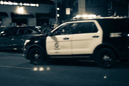 A black and white photograph depicts an Los Angeles Police Department SUV at night