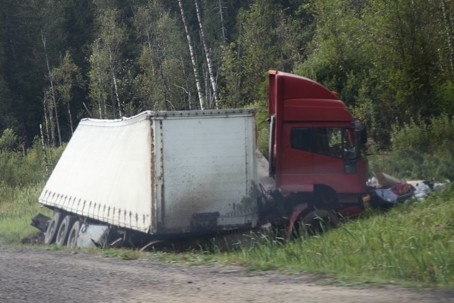 A red semi-truck rests off the road in a ditch, following a collision