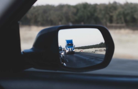 A car's side mirror reflects a large semi-truck