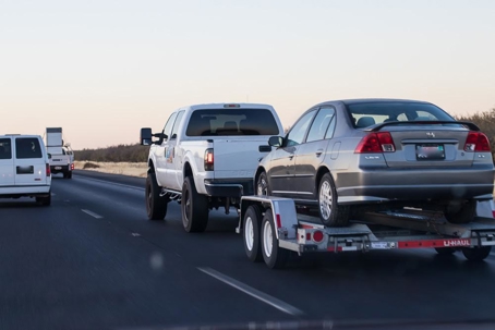 white pickup hauling a gray sedan