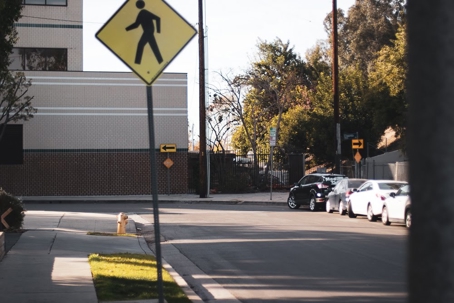 A street scene showing parked cars and a pedestrian crossing sign