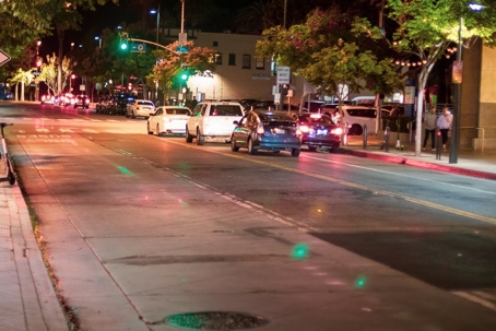 A nighttime street shows cars stopped at a green light