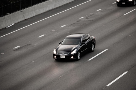 A dark car drives on a multilane highway.