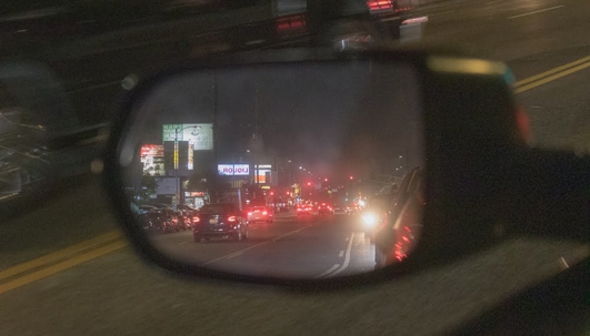 A car's side mirror reflects the city street at night