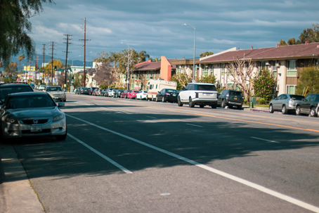 A long, straight street stretches into the distance with parked cars